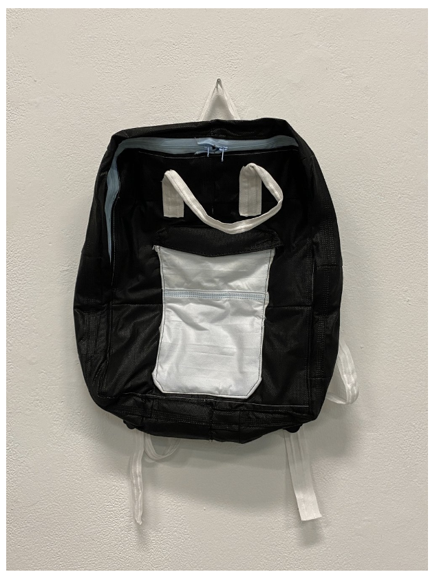 A black and white backpack made from medical masks hangs from a white wall.